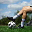 IDA Classica 22 Women's Soccer Cleat, Black and Red, FG/AG, Firm Ground, Artificial Ground, player sitting on a bench at soccer field with right foot balanced on a soccer ball