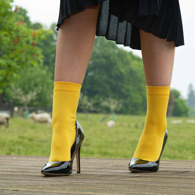 Woman wearing black high heels, a black skirt and Peper Harow yellow Classic women's luxury socks