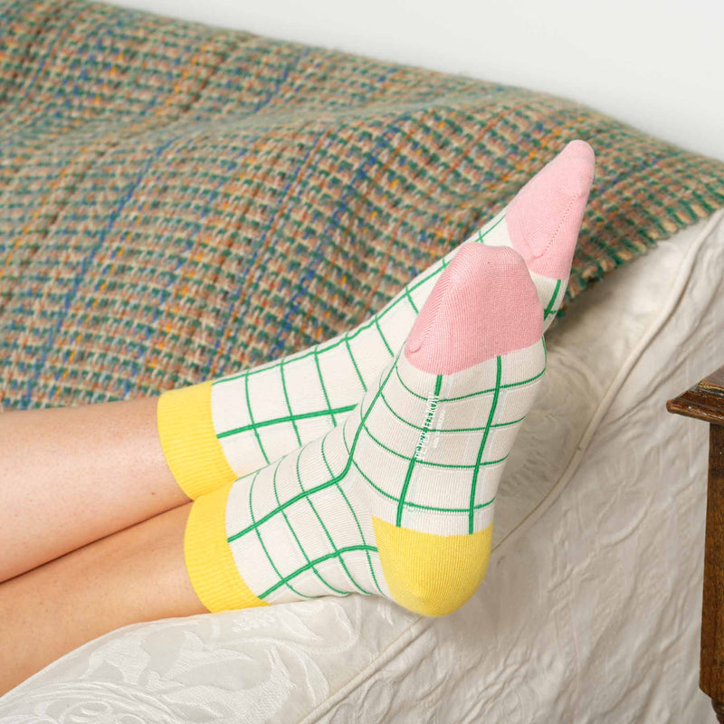 Woman sitting on a sofa wearing cream Grid luxury women's socks from Peper Harow