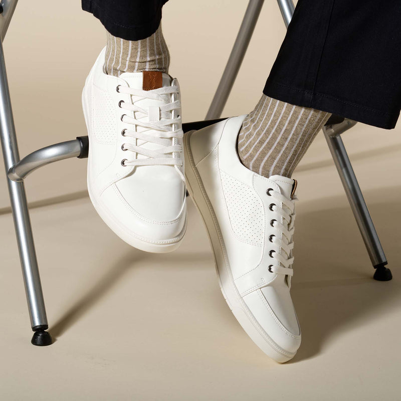 Man sitting on a stool wearing white trainers, black trousers and beige Recycled Ribbed men's recycled cotton socks by Peper Harow