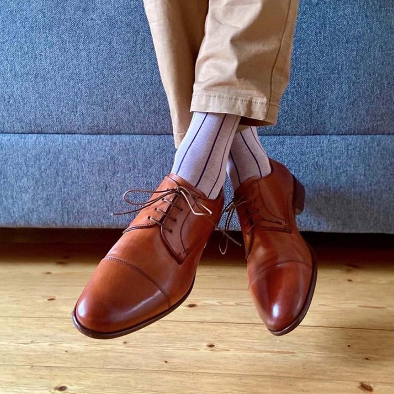 Man sitting on sofa wearing tan trousers, brown oxfords and pink Pin Stripe men's luxury socks by Peper Harow